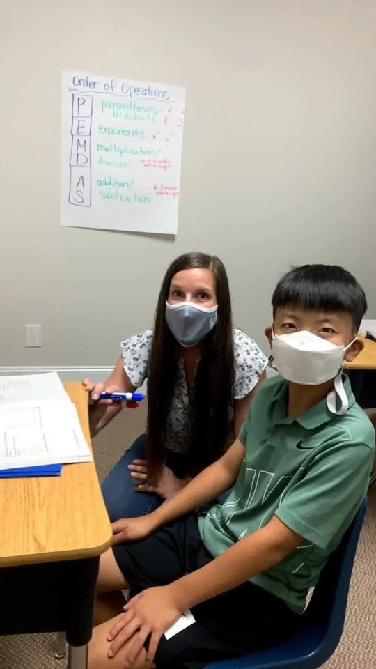 A tutor and student work together at a desk with an Order of Operations poster